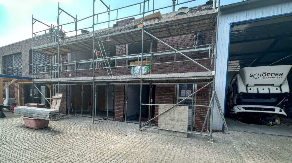 Ein im Bau befindliches Schöpper Backsteingebäude, vor dem Gerüste und Baumaterialien zu sehen sind.