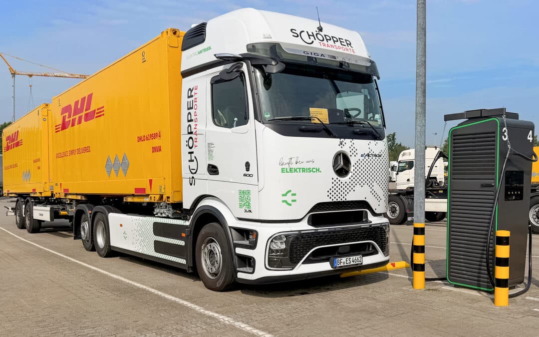 Ein weißer Elektro-Sattelzug mit einem gelben DHL-Anhänger lädt an einer Ladestation auf dem Schöpper Transporte Gelände.