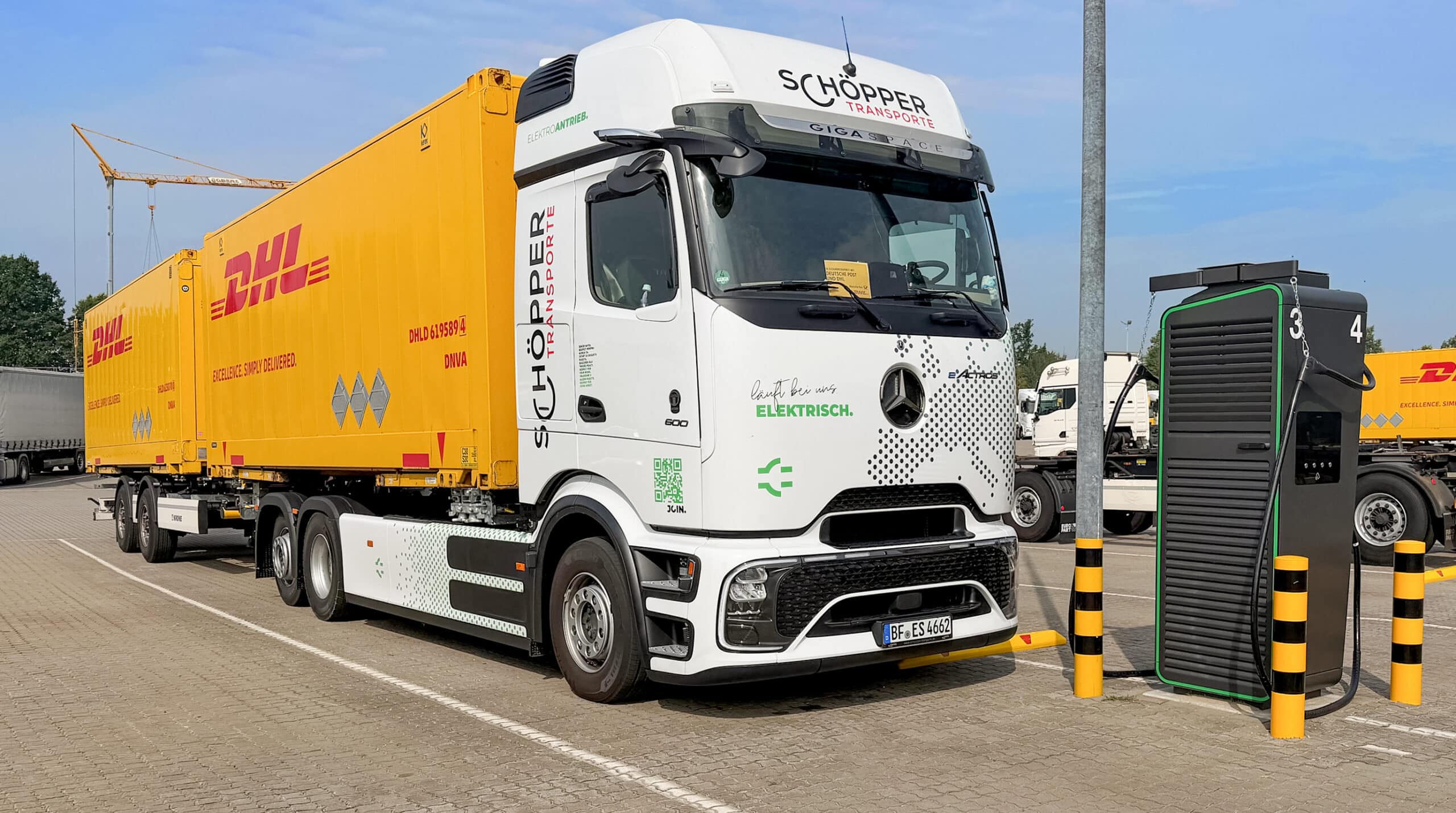 Ladeunkt auf dem Betriebsgelände der Schöpper Transport GmbH in Greven Ein weißer Elektro-Sattelzug mit einem gelben DHL-Anhänger lädt an einer Ladestation auf dem Schöpper Transporte Gelände.